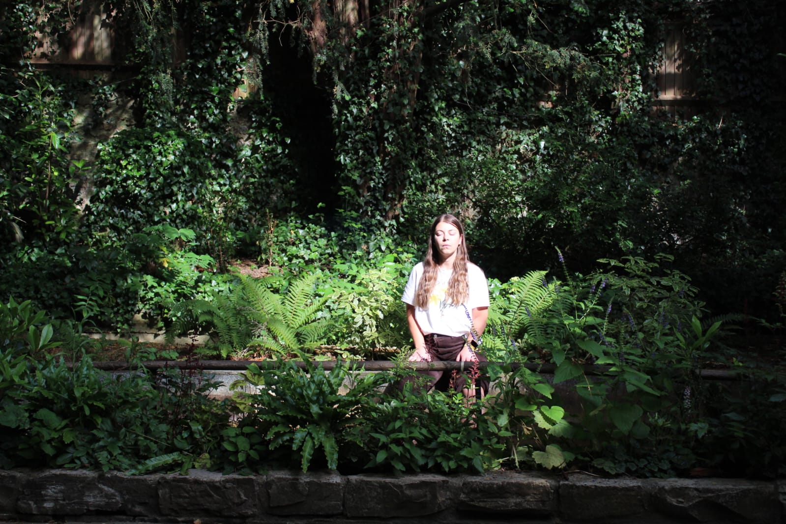 Ariela sentada en un jardín frondoso, rodeada de plantas y luz natural