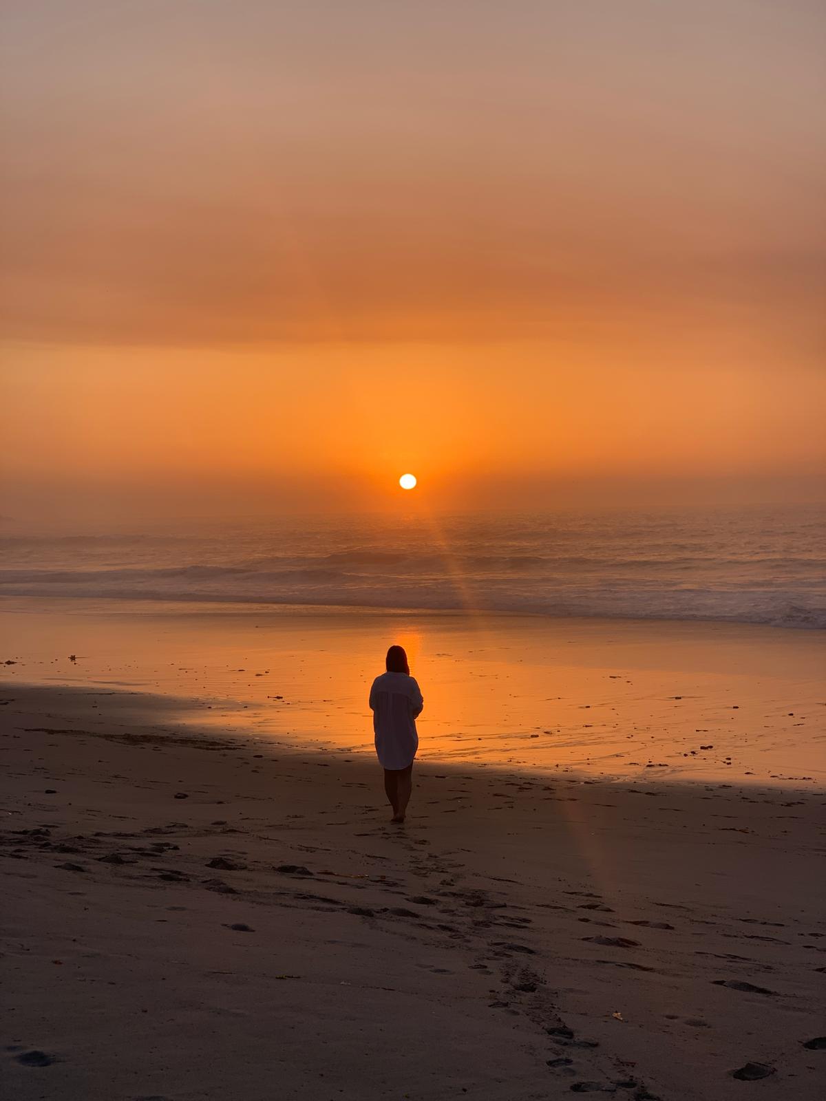 Ariela caminando en la playa frente al mar durante un atardecer dorado