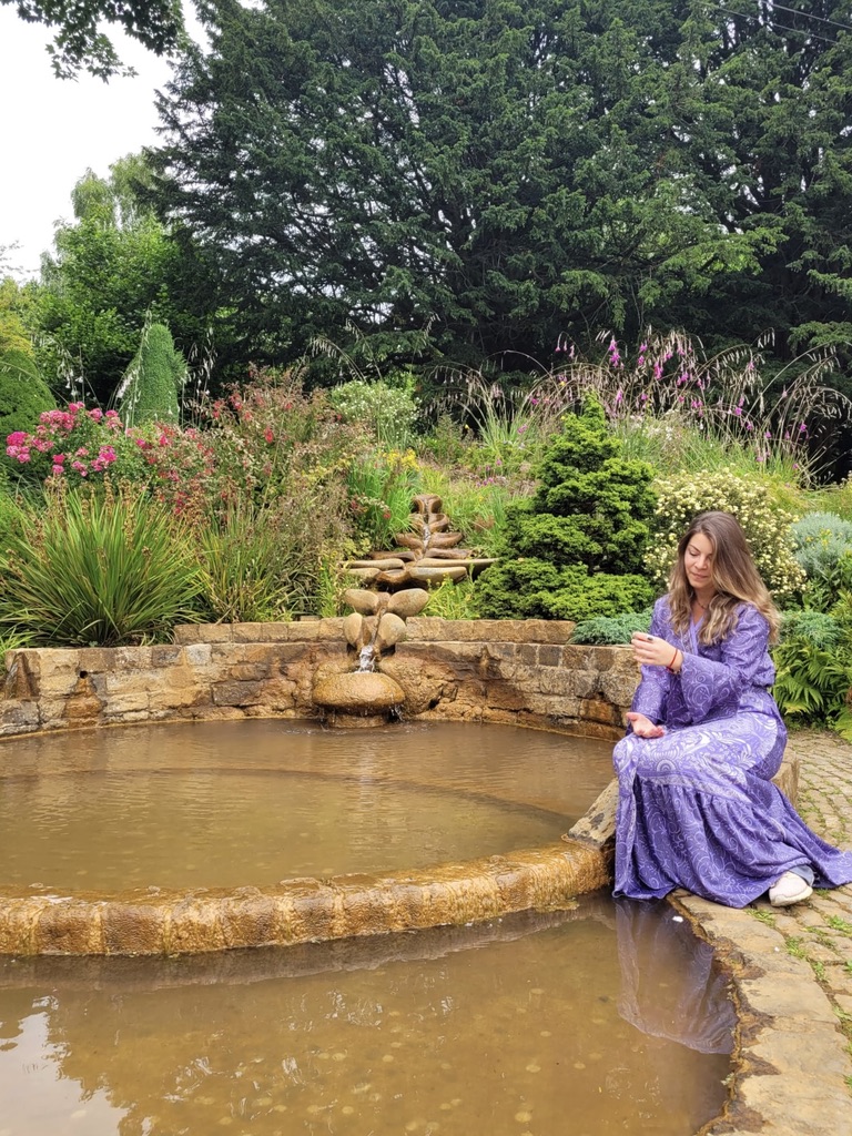 Ariela junto a una fuente rodeada de flores en Avalon