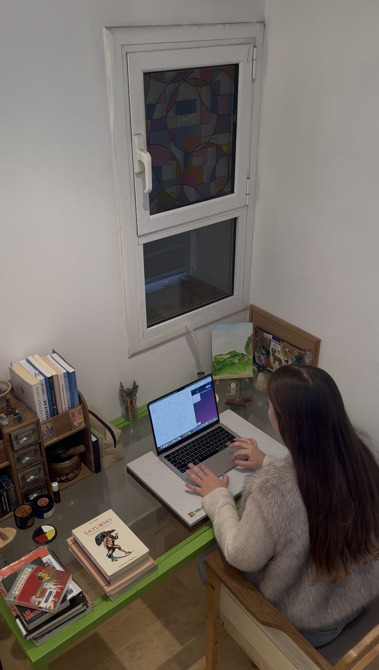 Ariela trabajando con una carta natal en el portátil, rodeada de libros y objetos de su espacio de consulta