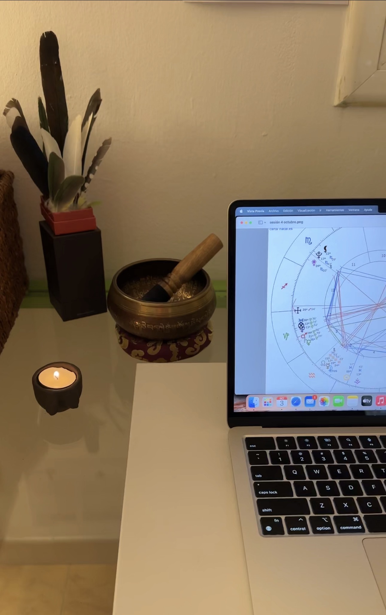 Detalle de una carta natal abierta en el portátil junto a una vela, un cuenco y plumas